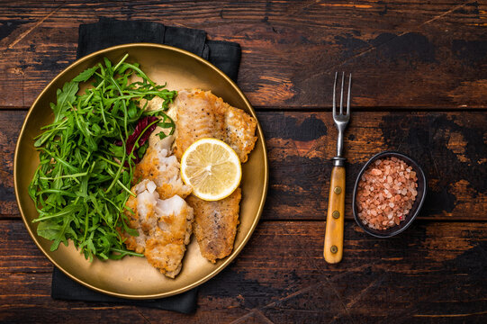 Roasted Pollock fish fillet on a plate with salad. wooden background. top view