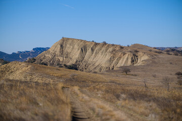 Dusty Dirt Road Through Dry Hills With Sparse Trees Under Clear Blue Sky in Vashlovani National Park, Georgia 2025 autumn