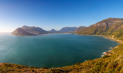 Stunning panoramic view of Hout Bay and coastal mountains from Chapman&rsquo;s Peak view point, Cape Town, Western Cape, South Africa. A blue bay, rugged peaks, South African scenery beneath a blue sky.