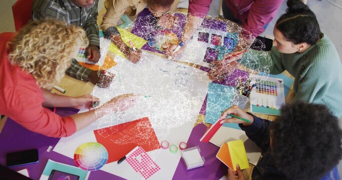 Collaborating design team leaning around table in studio, passing color wheel and paint samples