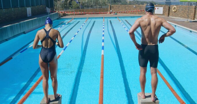Standing swimmers in swimwear adjusting goggles on starting blocks at outdoor pool, with lane ropes - Powered by Adobe