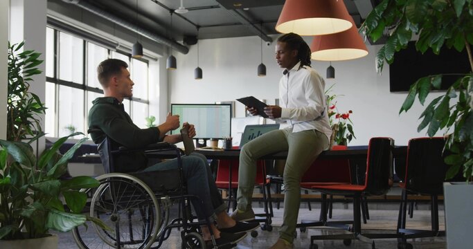 Discussing two colleagues wearing business casual sharing ideas in office, with wheelchair tablet - Powered by Adobe
