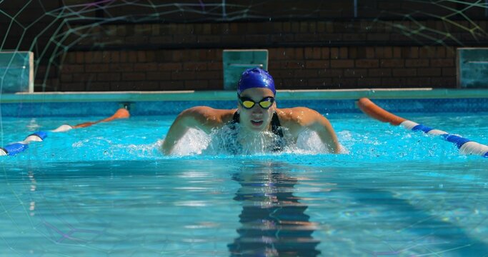 Emerging female swimmer propelling in outdoor pool lane, with black swimsuit, swim cap and goggles