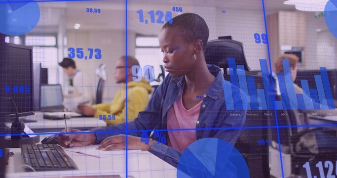 Writing woman in denim shirt taking notes at office workspace, with notebook monitor data overlay