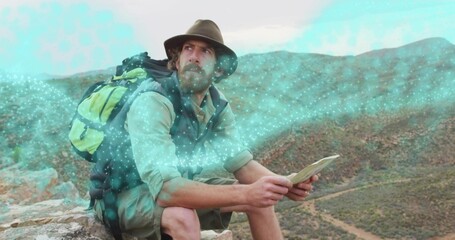 Sitting lone male hiker surveying canyon ledge, with map, green black backpack, wide-brimmed hat