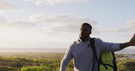 Signaling man in collared shirt and sweater carrying green backpack on coastal path, copy space