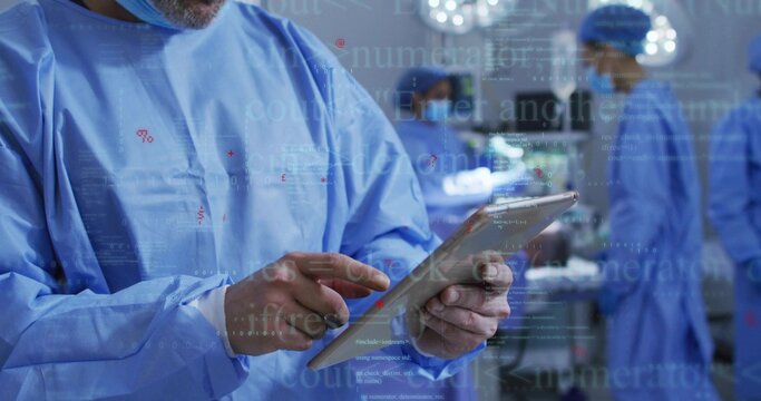 Reviewing surgeon in blue gown holding tablet in operating room, with monitors, surgical lights