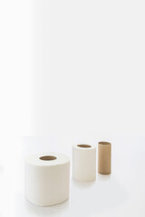 Vertical image. Close up of three rolls of toilet paper, one of them empty. on a white background, with huge copy space on top. Concept: "Some pretty useful is running out"