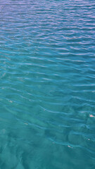A close-up view of calm turquoise ocean water under sunlight, showing gentle ripples and soft reflections on the surface, capturing the peaceful and clear tropical sea atmosphere.