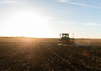 Fototapeta premium Farmer with tractor seeding in sunset
