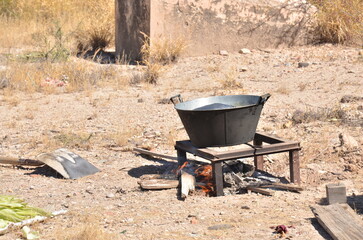 Rustic outdoor cooking scene with metal pot over open fire in arid landscape, evoking tradition and rural life with a touch of adventure and simple living