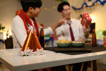 A party hat takes focus as joyful colleagues celebrate Christmas on the final workday with beer,...