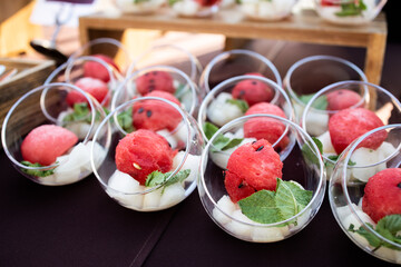 Elegant presentation of watermelon and melon cubes in clear glass bowls, garnished with fresh mint leaves. A refreshing summer dessert arrangement, perfect for a catering event or buffet.