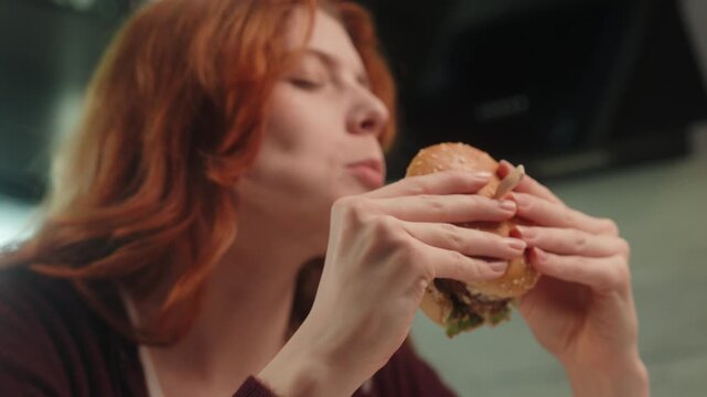 Caucasian woman female girl eating hamburger with eyes closed feeling delight enjoying fast takeaway junk food addiction bad habit meal biting cheeseburger dinner unhealthy snack relaxing at home