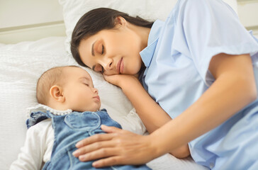 A tender mother rests beside her sleeping baby on a bed, gently touching the infant, sharing a...