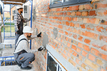 Builders applying plaster to brick wall construction site