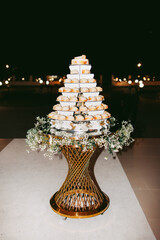 The bride's cake, gold stand decorated with flowers. There are white chocolate chip cookies on every shelf. The cakes are decorated with gold leaf.