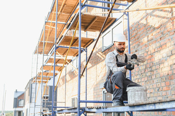 Construction worker pointing brick wall on scaffolding
