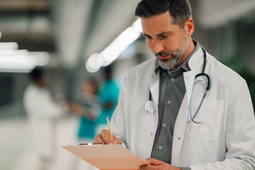 Male doctor writing on clipboard in hospital