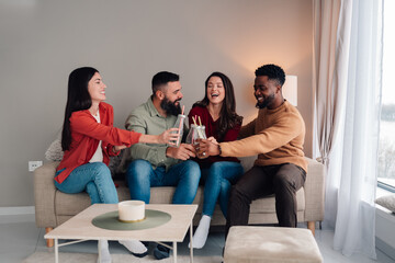 Diverse friends laughing cheering drinks together at home