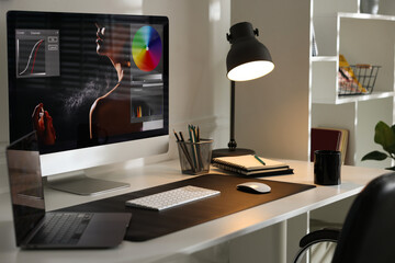 Stylish workplace with computer, laptop, cup, stationery and mat on desk, closeup