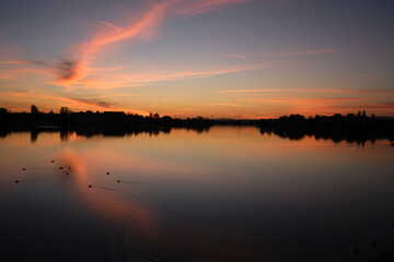 Red sunset over a tranquil lake, with fiery reflections glowing across the calm water surface.
