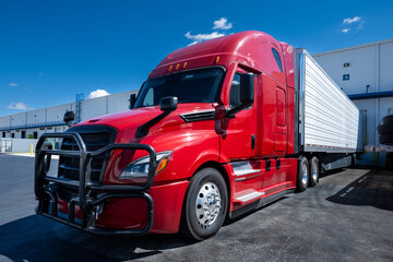 Red semi truck with trailer parked in warehouse loading dock