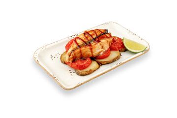 Grilled salmon fillet is served on a white plate with sliced tomatoes, potatoes and lime on a white isolated background. The concept is a delicious and healthy dish for culinary enthusiasts.