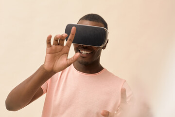 Young Black man interacting with virtual reality headset, smiling and reaching forward with both hands, engaging with immersive digital experience against neutral background