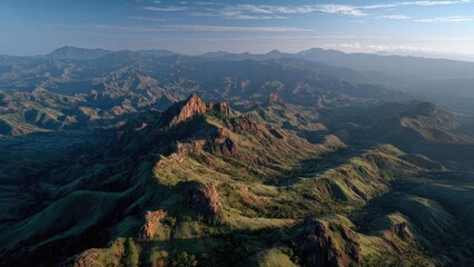 Fototapeta premium A vast green mountain landscape with rugged rocky peaks, rolling ridges and distant valleys under a clear blue sky. Concept Mountain Landscape, Rugged Peaks, Rolling Ridges, Distant Valleys