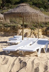 Empty plastic loungers and thatched umbrella on beach sand