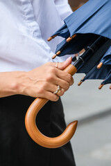 Close-up of female hands closing a blue umbrella outdoors.