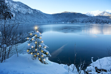 Christmas tree with lights and mountain reflection in the lake.
