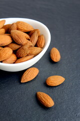 There is a bowl of almonds on a black background.