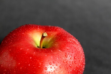 On a black background lies a whole red apple with splashes of water.