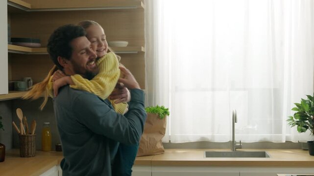 Caucasian family happy morning at home kitchen. Pensive man standing little daughter kid running to father daddy rise up baby spinning rotate turning around funny moment child girl hugging smiling