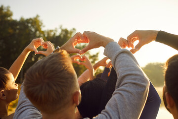 People making heart shape gesture with fingers in sunshine, back view. Crowd of happy young friends...