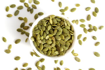 On a white background there is a white plate with green peeled pumpkin seeds.	