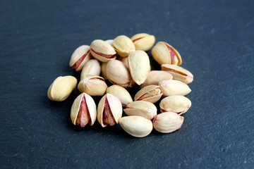 There is a small pile of pistachio nuts on a black background.