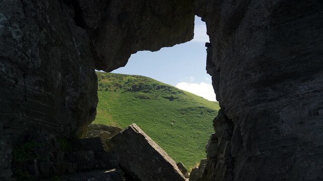 hidden cave overlooks lush landscape, remote cavern entrance showcases vivid green fields and azure