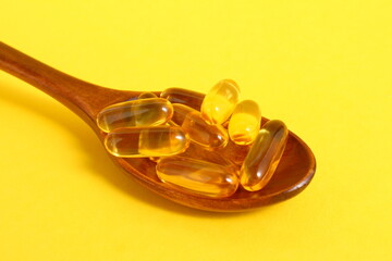 On a yellow background lies a pile of capsules with omega 3 vitamin on a wooden spoon.
