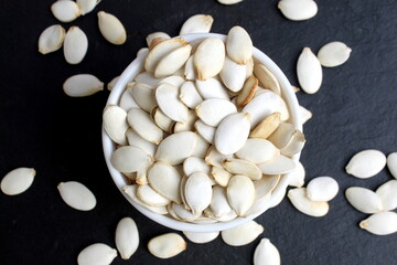 On a black background there is a bowl with unpeeled pumpkin seeds.	