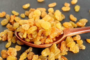 Yellow raisins lie on a wooden spoon on a black background.	