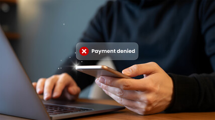 Hand Holding Smartphone with Glowing Payment Denied Notification Over Laptop Failure