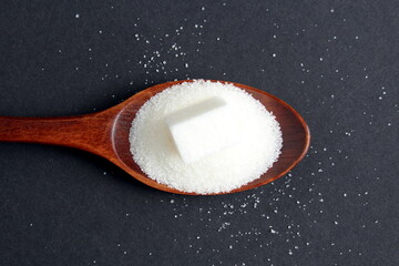 There is a wooden spoon with granulated sugar on a black background.
