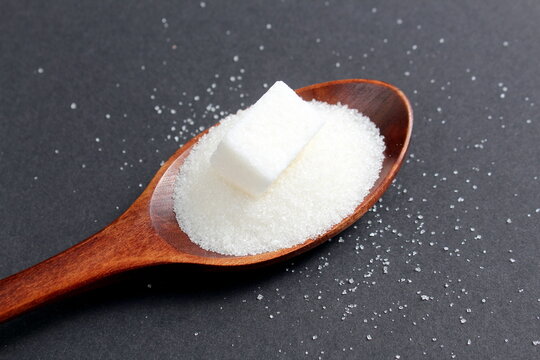There is a wooden spoon with granulated sugar on a black background.	