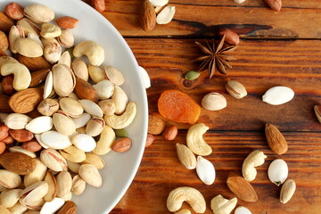 There is a plate with a pile of different nuts on the wooden table.