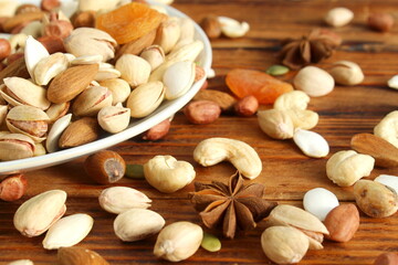 There is a plate with a pile of different nuts on the wooden table.	