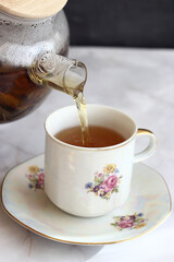 Green tea is poured into a cup from a transparent teapot