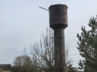 Old water tower standing tall among sparse trees in a rural landscape under a cloudy sky